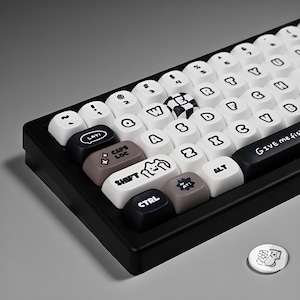 May include: A black and white mechanical keyboard with custom keycaps. The keycaps are white with black lettering and symbols, and some have unique illustrations. The keyboard includes a separate round button with a graphic. The text "GIVE me fish" is printed on the spacebar.