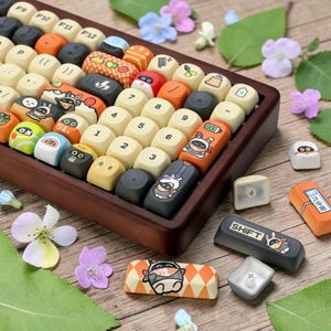 Könnte beinhalten: Eine individuelle mechanische Tastatur mit Holzrahmen und farbenfrohen Tastenkappen. Die Tastenkappen weisen verschiedene Designs auf, darunter Zeichentrickfiguren, geometrische Muster und Zahlen. Die Tastatur ist von Blumen und Blättern umgeben.