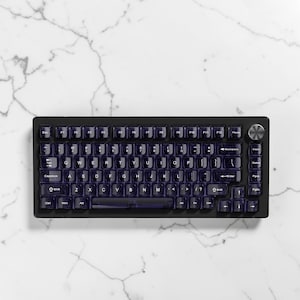 May include: A black mechanical keyboard with translucent purple keycaps. The keyboard has a compact layout with a silver volume knob and a white marble background. The keycaps are backlit.