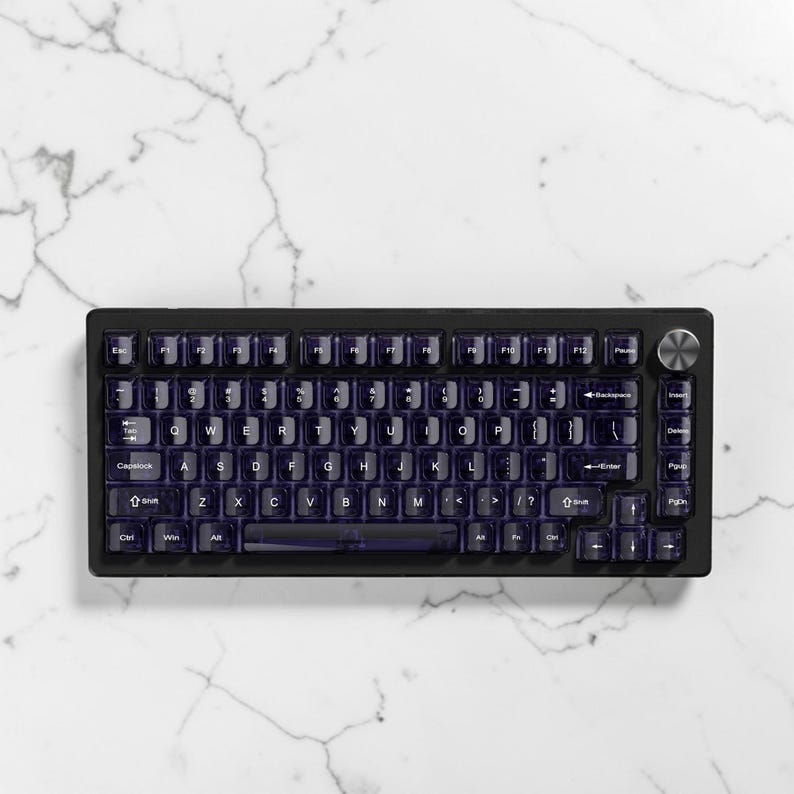 May include: A black mechanical keyboard with translucent purple keycaps. The keyboard has a compact layout with a silver volume knob and a white marble background. The keycaps are backlit.