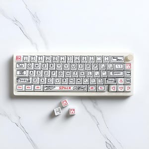 May include: A white mechanical keyboard with black and red accents. The keys are labeled with black text and hand-drawn style illustrations. The word "SPACE" is written in red on the space bar. Three loose keys are scattered below the keyboard.