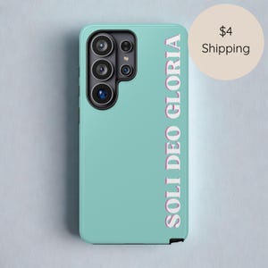 May include: A teal phone case with the text "SOLI DEO GLORIA" in a vertical, pink-outlined font. The case has a camera module on the upper left side.