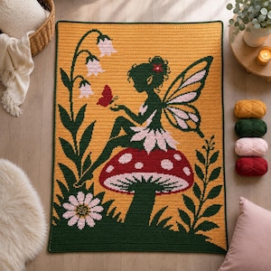 Puede incluir: Una manta de ganchillo rectangular con fondo amarillo que muestra a un hada de color verde oscuro sentada sobre una seta roja con puntos blancos. El diseño incluye una planta alta verde con flores rosas en forma de campana, una margarita y una mariposa roja.