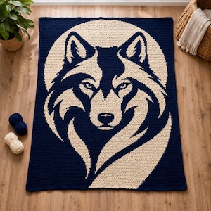 Puede incluir: Una manta rectangular de ganchillo que presenta un gran gráfico estilizado de una cabeza de lobo centrado en un fondo circular. El diseño utiliza un esquema de color de alto contraste en azul marino profundo y crema.