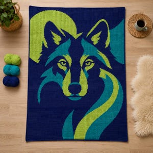 May include: A rectangular crochet blanket featuring a stylized wolf head graphic in shades of navy blue, lime green, and teal. The design displays a large circular shape behind the wolf, with the animal's face centered in a geometric pattern.