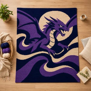 Puede incluir: Una manta de ganchillo rectangular que presenta un gran dragón morado con las alas extendidas sobre una luna circular de color crema. El fondo es azul marino oscuro con cintas de color crema que fluyen por la parte inferior del diseño.