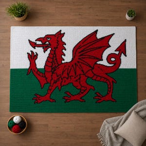 May include: A rectangular crochet rug featuring the Welsh flag design with a horizontal white top half and a green bottom half. A large, detailed red dragon is centered on the rug, depicted in a classic profile stance with wings spread.