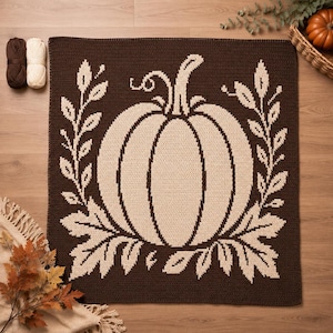 May include: A square crochet blanket featuring a large, centered cream-colored pumpkin design against a dark brown background. The pumpkin is flanked by two vertical leafy vine patterns, all rendered in a contrasting cream yarn on the dark brown base.