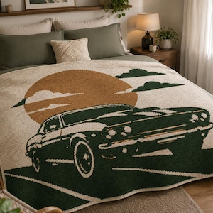 Puede incluir: Una manta color crema con un diseño de coche verde, un sol marrón y nubes verdes. La manta está sobre una cama con ropa de cama y almohadas verdes. El diseño de la manta presenta un coche antiguo.