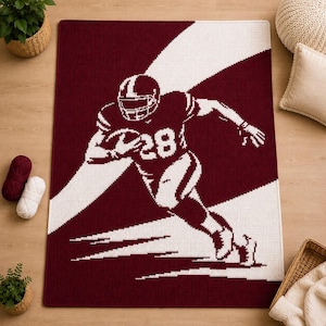 May include: A rectangular throw blanket featuring a maroon and white pixelated design of a football player in motion. The player wears a helmet and a jersey with the number 28, depicted in a high-contrast graphic style against a diagonal striped background.