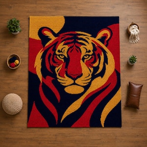 May include: A rectangular crochet rug featuring a large, centered tiger face graphic. The design uses a bold color palette of deep navy blue, vibrant red, and golden yellow, with the tiger's features rendered in a stylized, graphic pattern.