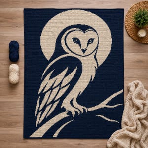 Può includere: Una coperta rettangolare all'uncinetto con uno sfondo blu navy scuro e un grande barbagianni color crema appollaiato su un ramo. Il gufo è centrato all'interno di un alone circolare color crema, creando un design grafico ad alto contrasto.