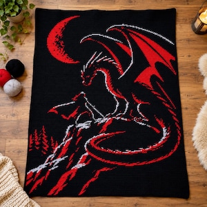 May include: A rectangular crochet blanket featuring a black background with a red and white graphic design of a dragon perched on a mountain peak under a crescent moon, with a forest silhouette visible at the base of the mountain.