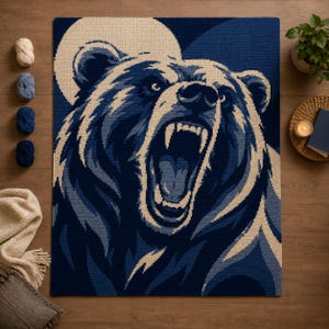 Puede incluir: Una manta de ganchillo rectangular con un gráfico grande y detallado de un oso rugiendo en tonos azul marino, azul claro y crema. El oso se muestra con la boca abierta, mostrando los dientes, sobre un fondo circular de color crema.