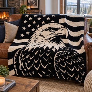 May include: A black and cream-colored knit throw blanket featuring a large graphic of a bald eagle head centered over a stylized American flag pattern with stars and horizontal stripes, draped over a brown leather sofa.