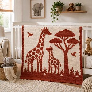 Könnte beinhalten: Eine cremefarbene Babydecke mit einem rostfarbenen Giraffen- und Baumdesign. Die Decke wird in einem weißen Kinderbett präsentiert, mit einem Giraffen-Spielzeug und einem gerahmten Elefanten-Druck im Hintergrund.