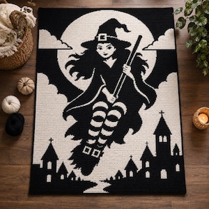 Puede incluir: Una alfombra rectangular de ganchillo en blanco y negro con un gráfico central de una bruja volando sobre una escoba frente a una gran luna llena. El diseño incluye siluetas de pequeños edificios en la parte inferior y nubes.