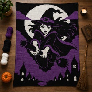 May include: A rectangular crochet blanket featuring a black, white, and purple graphic design of a witch flying on a broomstick in front of a large full moon. The scene includes a silhouette of a village with a church steeple at the bottom.