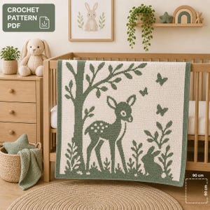 Op de afbeelding: Een crèmekleurige gehaakte babydeken met een bosgroen hert- en boomontwerp. De deken, 90 cm vierkant, heeft vlinders en een konijn. De tekst "CROCHET PATTERN PDF" staat in de linkerbovenhoek. De deken is over een houten ledikant gedrapeerd.