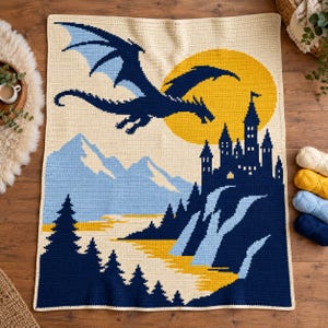 May include: A rectangular crochet blanket featuring a dark blue dragon flying in front of a large yellow sun. The scene includes a dark blue castle on a cliff, light blue mountains, a yellow river, and dark blue pine trees on a cream background.