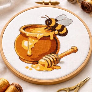 May include: Cross-stitch embroidery of a honey pot with dripping honey and a bee. The pot is orange and the bee is black and yellow. A wooden honey dipper rests beside the pot. The embroidery is set in a wooden hoop.