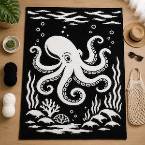 Puede incluir: Una manta de ganchillo rectangular con un diseño de alto contraste en blanco y negro. El gráfico central muestra un pulpo grande rodeado de burbujas, algas y formaciones de coral. El patrón de puntos crea una superficie texturizada.