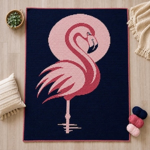May include: A rectangular crochet blanket featuring a large pink flamingo centered against a circular light pink background on a dark navy blue field. The blanket has a thin red border and displays a stylized bird with a dark beak and one leg.