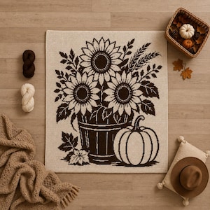 May include: A rectangular crochet blanket featuring a dark brown graphic design on a cream background. The pattern depicts a bucket filled with three large sunflowers and foliage, accompanied by a pumpkin and fallen leaves at the base.