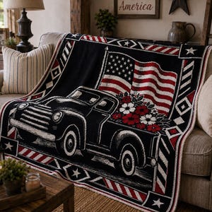 May include: A black throw blanket draped over a sofa, featuring a vintage truck design with an American flag and floral arrangement. The blanket has red, white, and black accents.