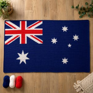 May include: A rectangular crochet rug featuring the Australian flag design in dark blue, red, and white. The pattern includes the Union Jack in the upper left corner, a large seven-pointed Commonwealth Star below it, and the Southern Cross constellation.