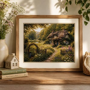 May include: A framed print of a cottage scene with a thatched roof, surrounded by lush greenery and flowers. The artwork is set in a wooden frame and rests on a wooden surface, alongside books and a decorative house.