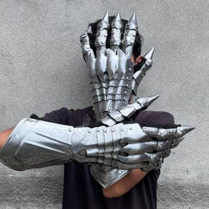 May include: Silver-colored, articulated gauntlets and hand armor with sharp, pointed spikes. The armor covers the hands, wrists, and forearms, with detailed segmented plates. The overall design suggests a fantasy or cosplay theme.