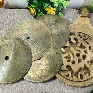 Puede incluir: Una colección de astrolabios y discos antiguos de latón con intrincados diseños grabados. Los instrumentos, de varios tamaños, están dispuestos sobre una superficie de piedra, mostrando su detallada artesanía y significado histórico.
