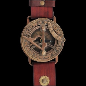 Puede incluir: Un reloj de brújula de estilo vintage con esfera de color bronce y correa de cuero rojo oscuro. La esfera del reloj presenta números romanos, una rosa de los vientos y el texto "West London". La correa está asegurada con remaches.