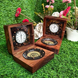 May include: Two square wooden boxes with hinged lids, each containing an analog clock on the inside lid and a circular compass set into the base. The clock faces feature Roman numerals and the text 49 Bond Street London.