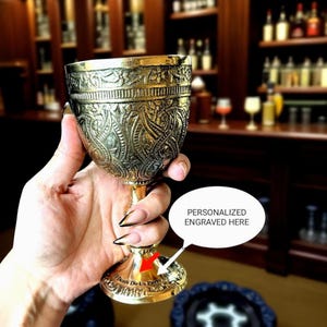 Könnte beinhalten: Verziertes goldfarbenes Kelch mit aufwendigen geprägten Mustern. Der Stiel und der Sockel sind ebenfalls mit Designs versehen. Der Sockel trägt den Text "Death Do Us Part". Eine Sprechblase sagt "PERSONALISIERT GRAVIERT HIER".