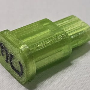 May include: A translucent green plastic object with a rectangular shape and a cylindrical extension. The object has the number "30" written on it in black marker. The object is likely a 3D-printed part.