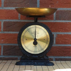 May include: A vintage Salter Family Scale No. 45 with a black cast iron base and a circular brass face. The scale features a large brass weighing bowl on top, a black needle pointing to zero, and markings in both kilograms and pounds.