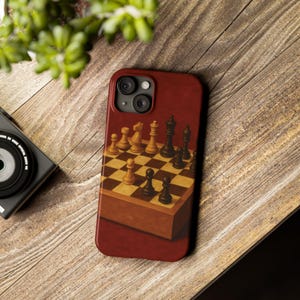 Puede incluir: Una funda de teléfono burdeos con un diseño detallado de tablero de ajedrez. Las piezas de ajedrez están dispuestas en un tablero a cuadros, con una base de caja de madera. La funda está sobre una superficie de madera.