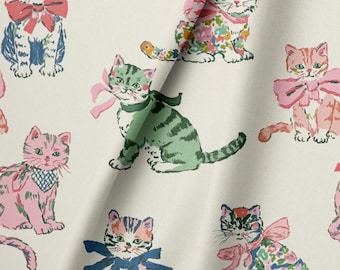 May include: A light-colored fabric featuring a repeating pattern of illustrated cats in various colors, including pink, green, and blue. Each cat is adorned with a bow or a patterned neck accessory, rendered in a hand-drawn style with visible ink lines.