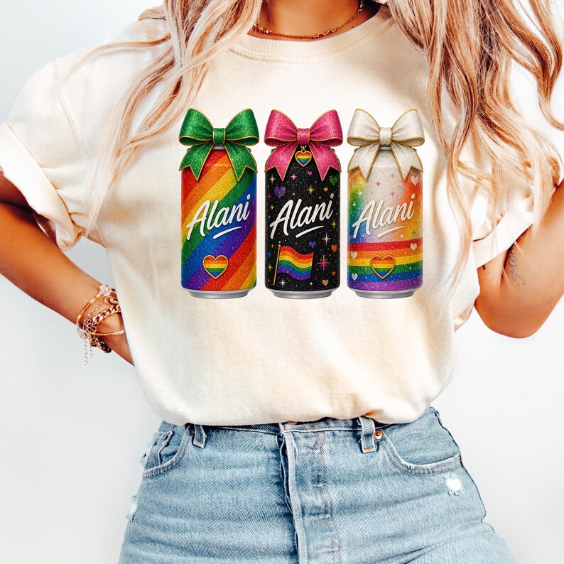 Pu&ograve; includere: Una maglietta color crema con tre lattine di bevande con disegni arcobaleno, neri e arcobaleno. Ogni lattina ha un fiocco in cima e la parola "Alani" stampata sul davanti. La maglietta &egrave; indossata da una persona in jeans blu.