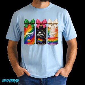 Pu&ograve; includere: T-shirt azzurra con tre lattine colorate con fiocchi. Ogni lattina ha la scritta "Alani" e un cuore arcobaleno. Le lattine hanno sfondi arcobaleno, neri e bianchi.