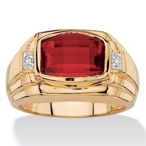 May include: A gold-toned ring with a large, rectangular, faceted red gemstone as the centerpiece. Small, square, diamond-like accents flank the red stone. The ring has a wide band with a classic, elegant design.