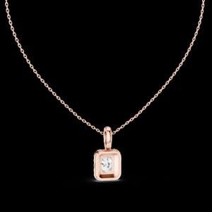Może przedstawiać: Naszyjnik z r&oacute;żowego złota z kwadratową zawieszką z przezroczystym, kwadratowo oszlifowanym kamieniem szlachetnym. Zawieszka jest osadzona w oprawie z lunetą i wisi na delikatnym łańcuszku. Naszyjnik jest prezentowany na czarnym tle.