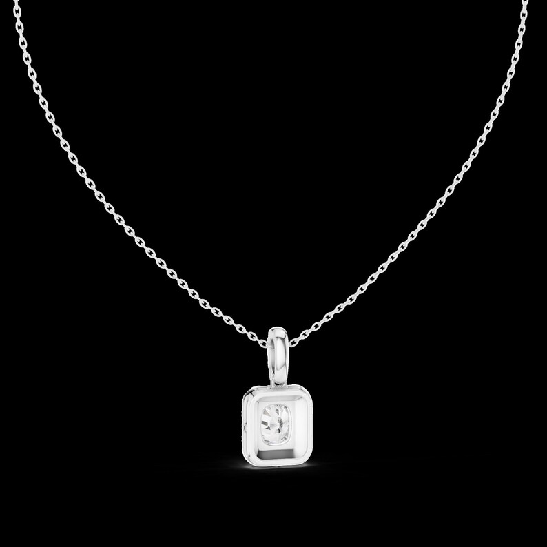 Może przedstawiać: Srebrny naszyjnik z kwadratową zawieszką z przezroczystym, okrągłym kamieniem szlachetnym. Zawieszka jest osadzona w kwadratowej ramie i wisi na delikatnym łańcuszku. Tło jest czarne.