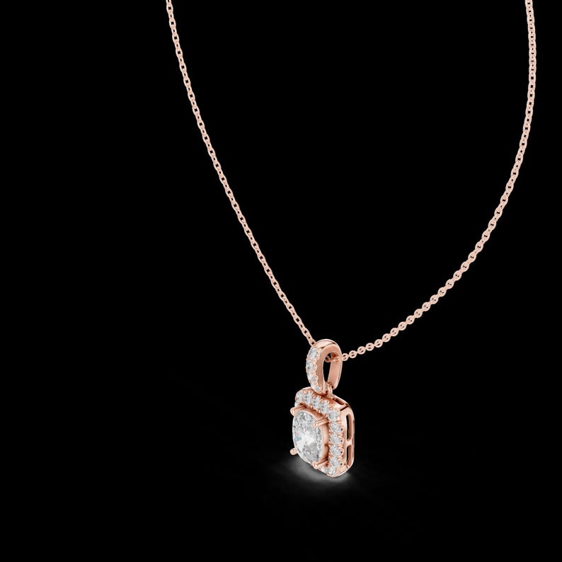 Może przedstawiać: Naszyjnik z wisiorkiem z r&oacute;żowego złota z kwadratowym diamentem otoczonym mniejszymi diamentami. Wisiorek zawieszony jest na delikatnym łańcuszku. Biżuteria jest umieszczona na czarnym tle.