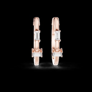 Può includere: Orecchini a cerchio in oro rosa con tre pietre preziose rettangolari e trasparenti. Gli orecchini hanno una finitura lucida e un design semplice. Le pietre sono distanziate uniformemente.