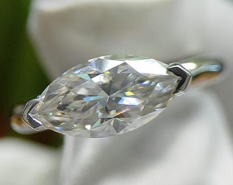 May include: A marquise-cut diamond ring with a silver band. The diamond is the focal point, reflecting light with many facets. The ring is held against a white background, with the brand name "SKYLINKJEWEL" visible.