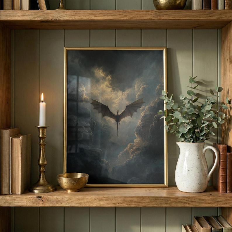 May include: A framed print depicting a dragon in flight against a backdrop of dramatic clouds. The gold-framed artwork is displayed on a wooden shelf with books, a candle, and a decorative bowl. The dragon is silhouetted against the sky.