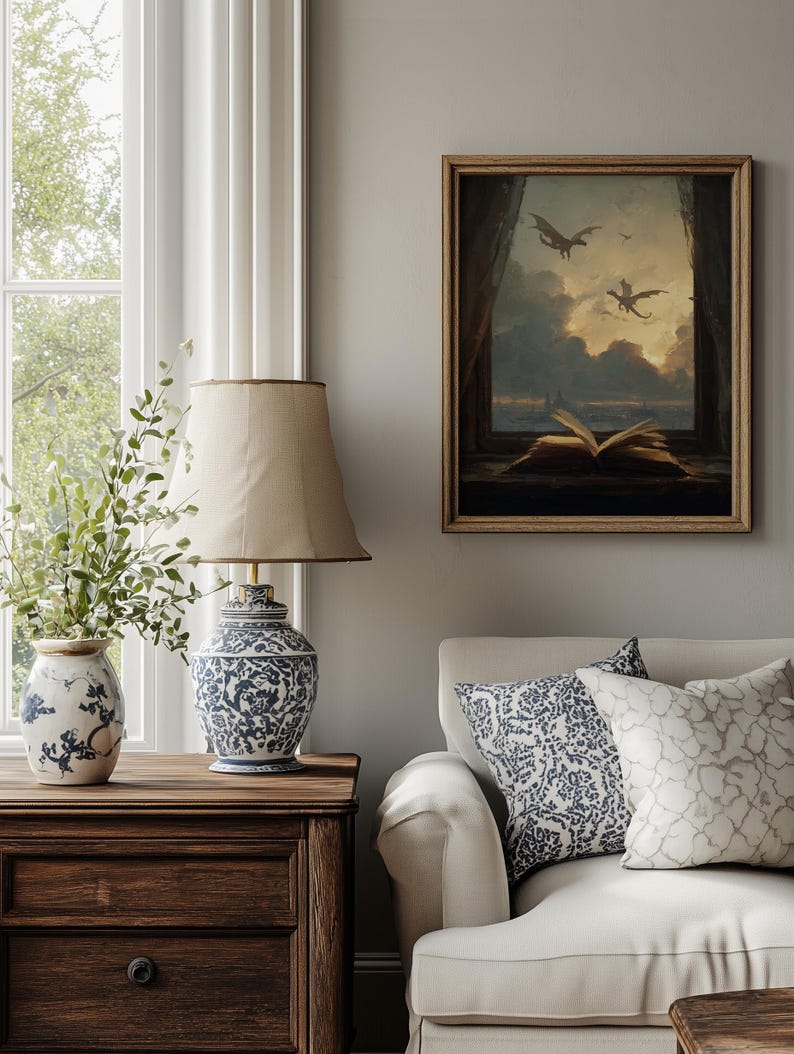May include: A cozy living room scene featuring a framed artwork with dragons flying in a cloudy sky. A blue and white patterned lamp sits on a wooden nightstand, next to a vase with greenery. A white sofa with patterned pillows completes the scene.